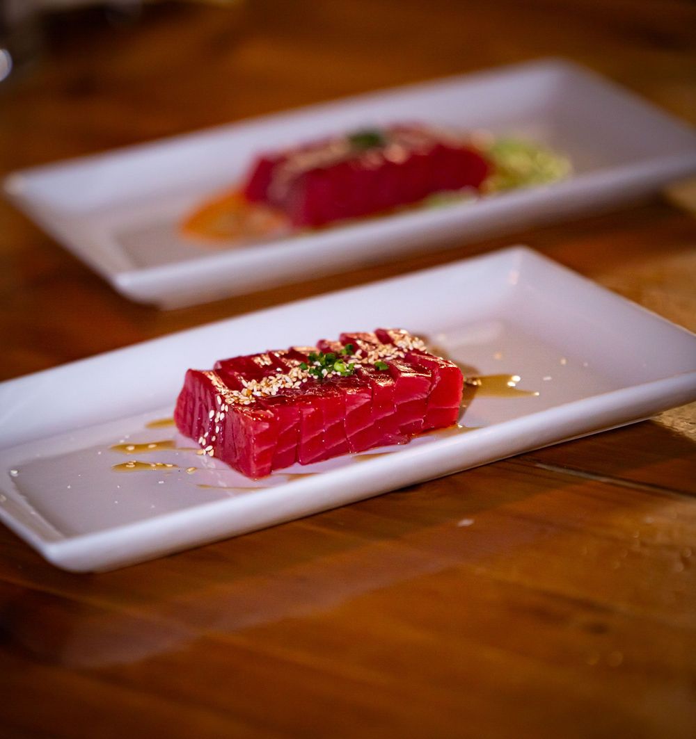 Fresh raw tuna sashimi being plated on long white rectangular dishes.