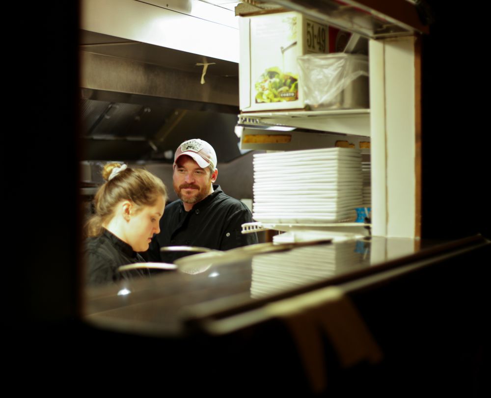 Dimly lit restaurant kitchen interior showing food preparation area through service window.