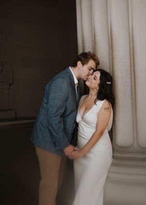 A romantic moment between a couple in formal wear standing by elegant columns.