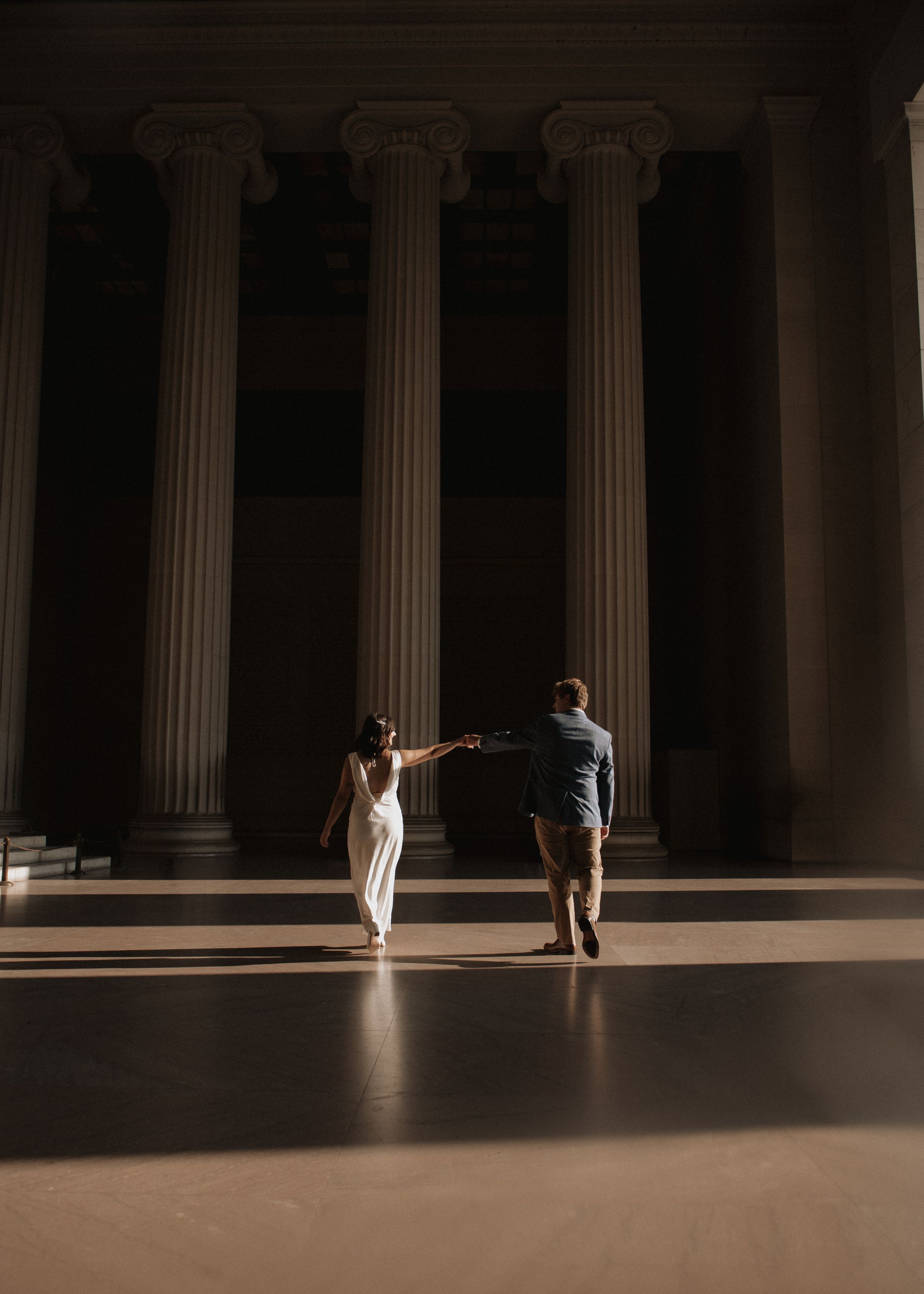 A couple dancing in a dramatic columned hall with moody lighting.