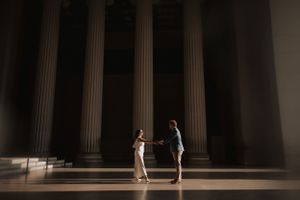 A couple shares an intimate moment between towering classical columns.