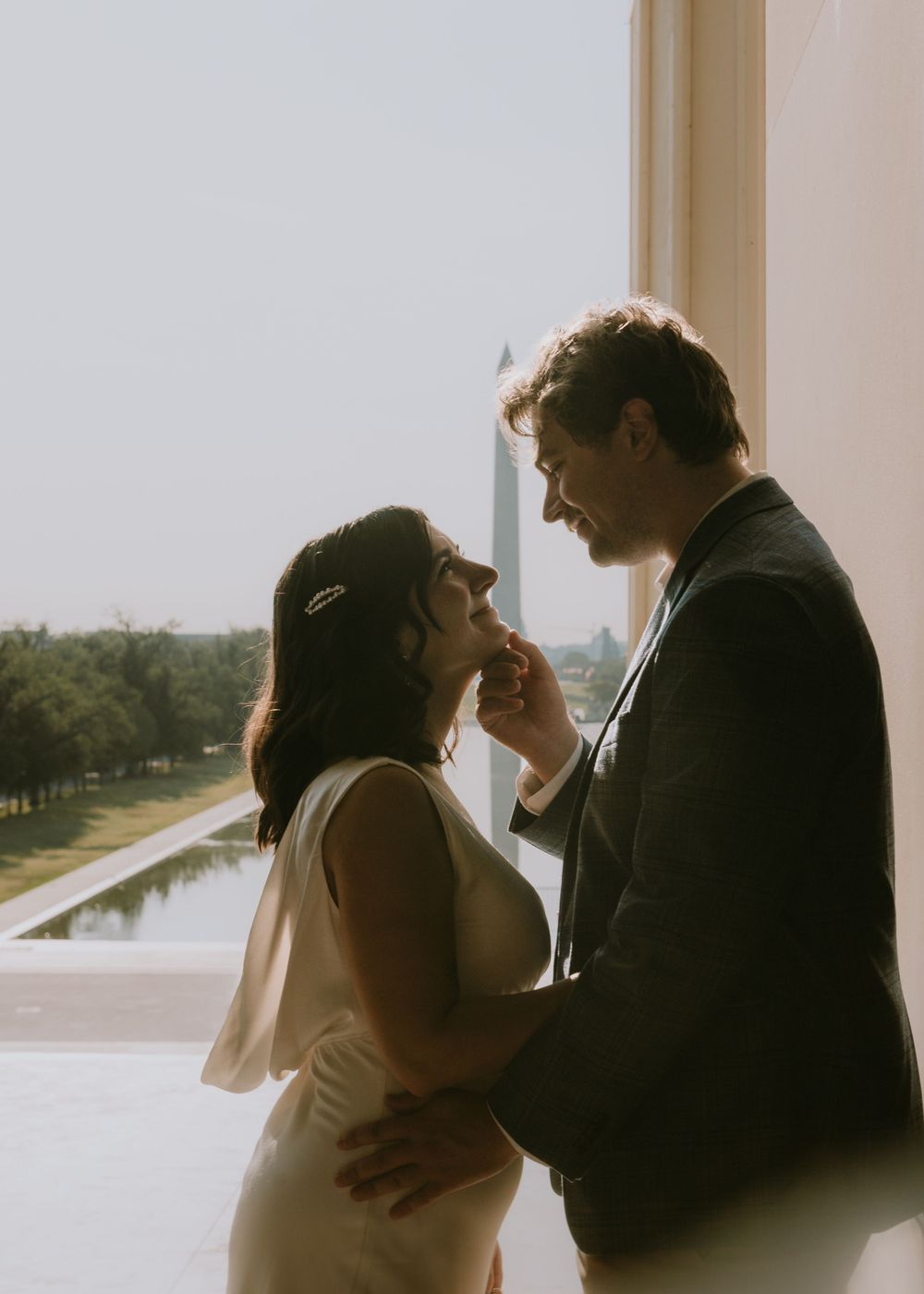 A tender moment between a couple by a window overlooking a reflecting pool.