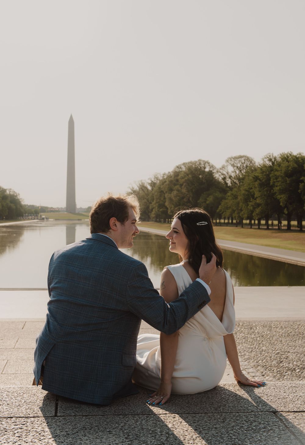 A couple sits by the Washington Monument reflecting pool on a sunny day.