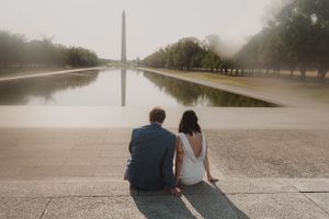 A couple sits together watching the Washington Monument across the reflecting pool.