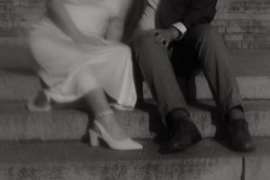 A couple sits on stone steps in an artistic black and white composition.