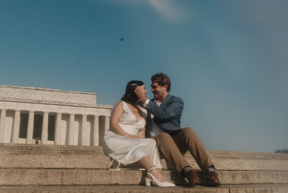 A couple sits on the Lincoln Memorial steps with the Washington Monument in the background.