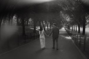Black and white photo of couple walking down tree-lined path together.