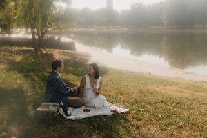 Couple enjoys intimate picnic by water with dreamy landscape backdrop.