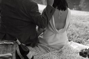 Black and white photo of couple sitting on blanket with wine bottle during picnic.