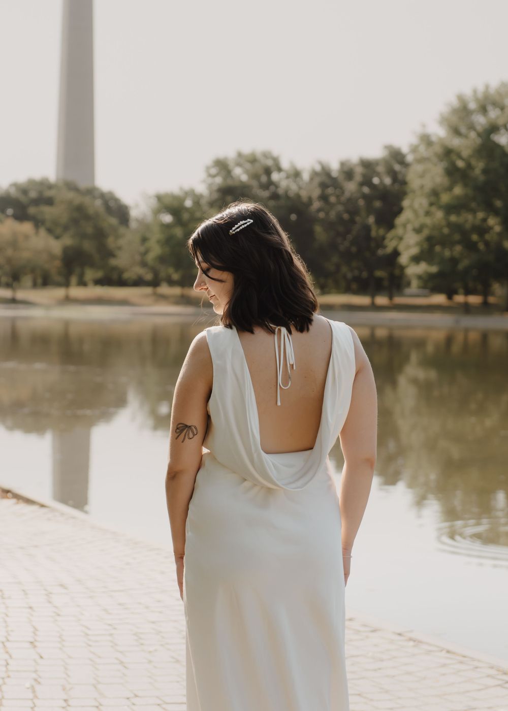 Woman in white dress standing by reflecting pool with Washington Monument in background.