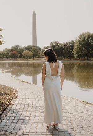 Back view of woman in flowing white dress near Washington Monument and reflecting pool.