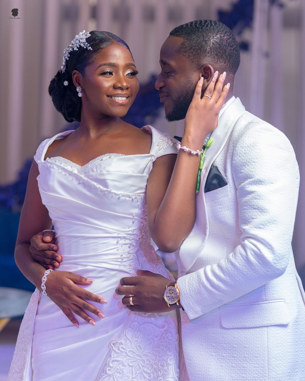 A romantic wedding moment as the couple embraces in matching white formal attire.
