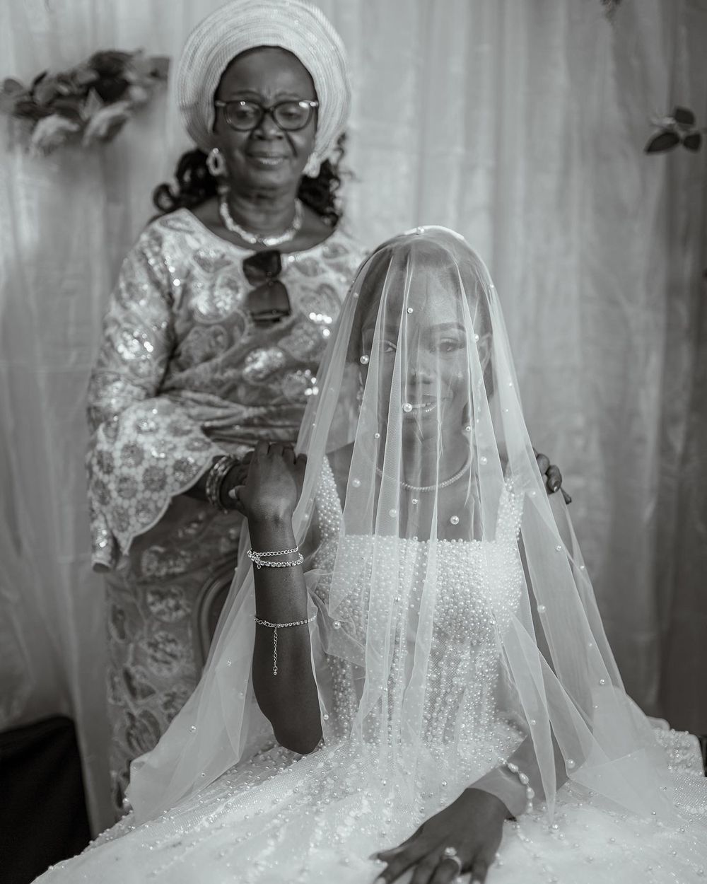 A black and white wedding photo showing preparations with traditional attire and a flowing veil.