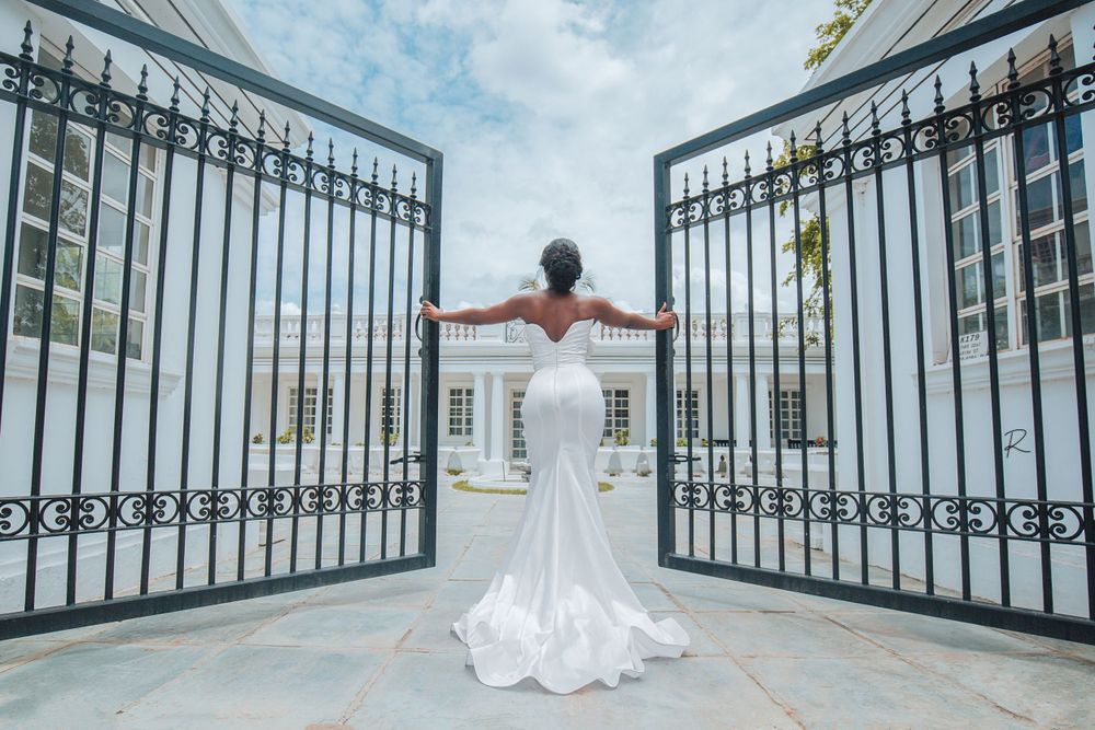 A bride in a fitted mermaid wedding dress poses dramatically between ornate iron gates.