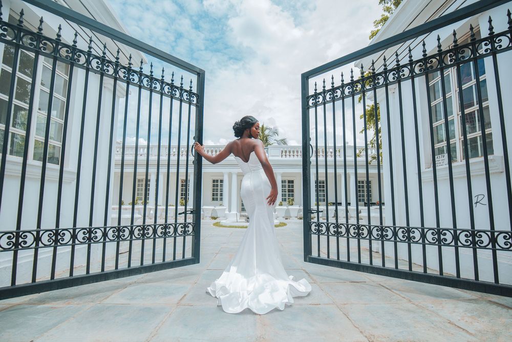 A bride stands elegantly between open iron gates in a form-fitting white wedding gown.