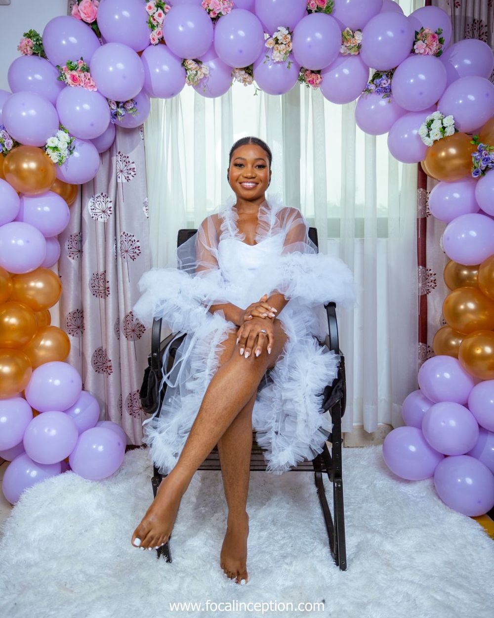 A glamorous bridal portrait under a purple and gold balloon arch with white tulle dress and flowing details.