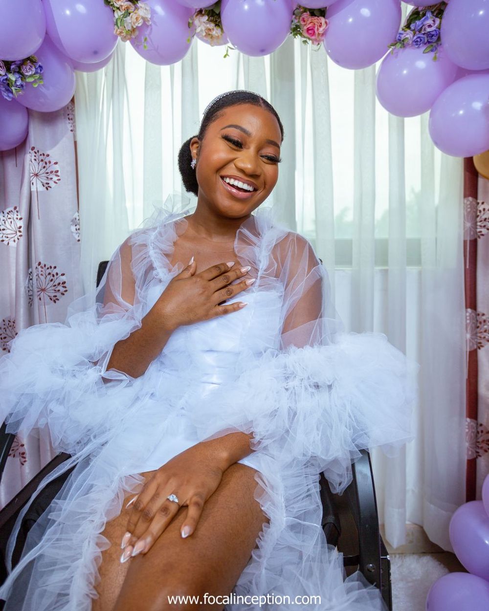 Elegant bridal portrait sitting in a chair surrounded by purple balloons and wearing a white tulle gown.
