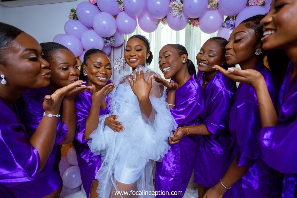 Fun group photo of bridesmaids in purple robes gathered around the bride in white.