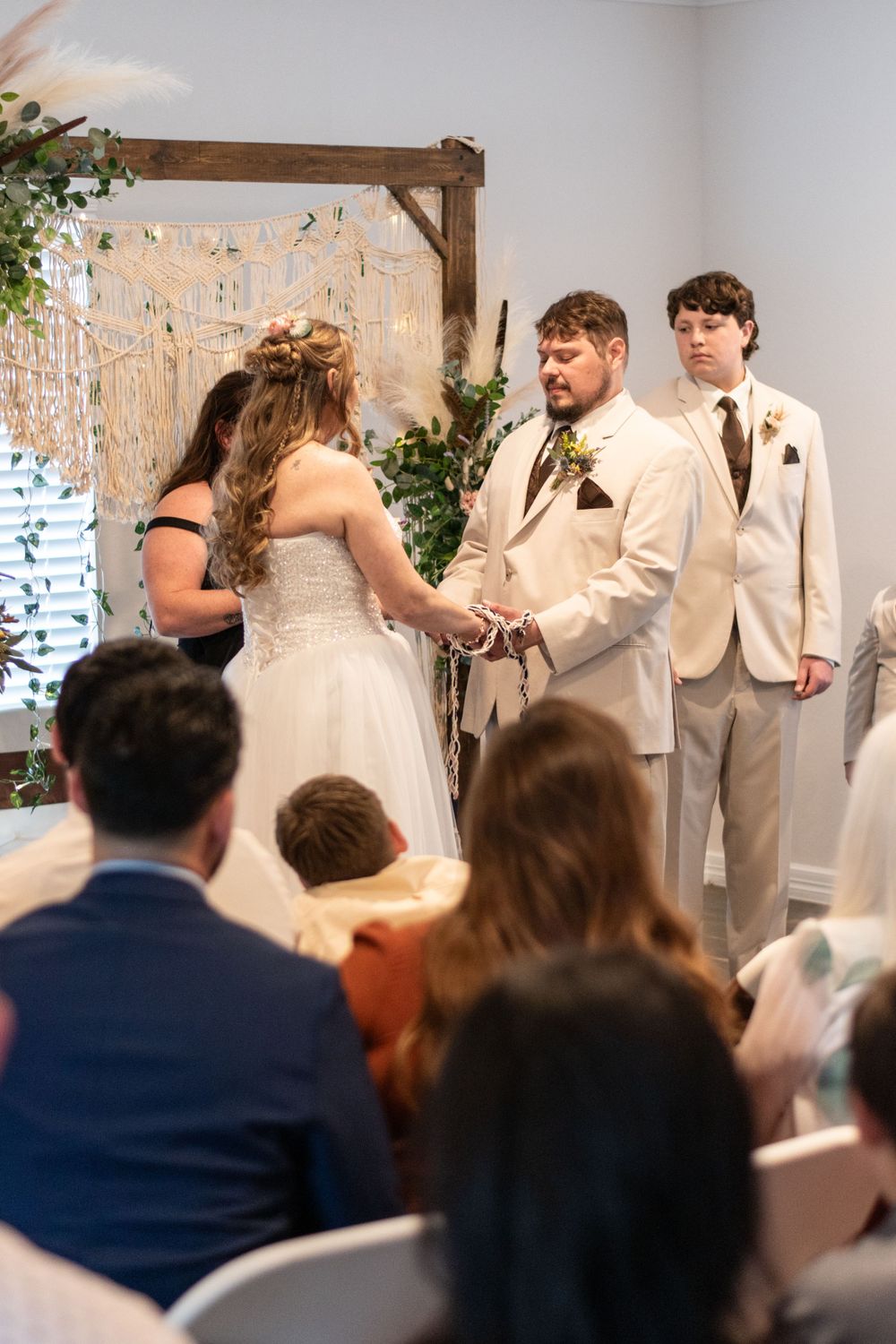 An intimate indoor wedding ceremony with guests watching as a couple exchanges vows in front of a decorative backdrop.