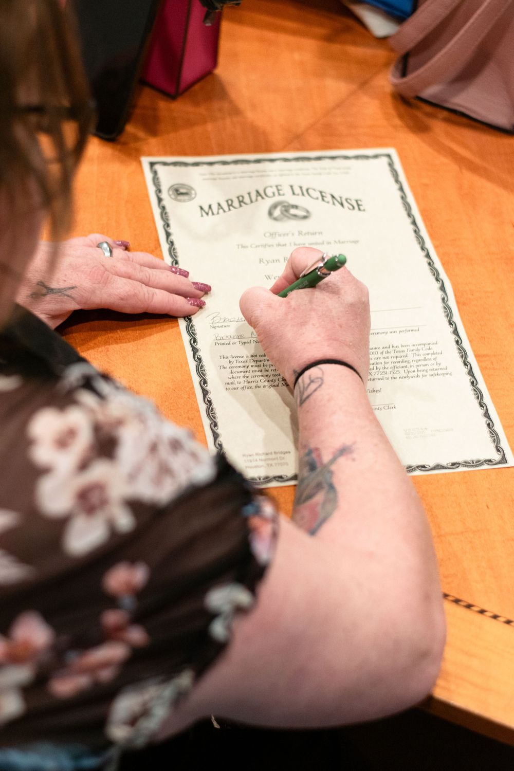 Someone signing a marriage license document on a wooden surface while wearing a floral print top.
