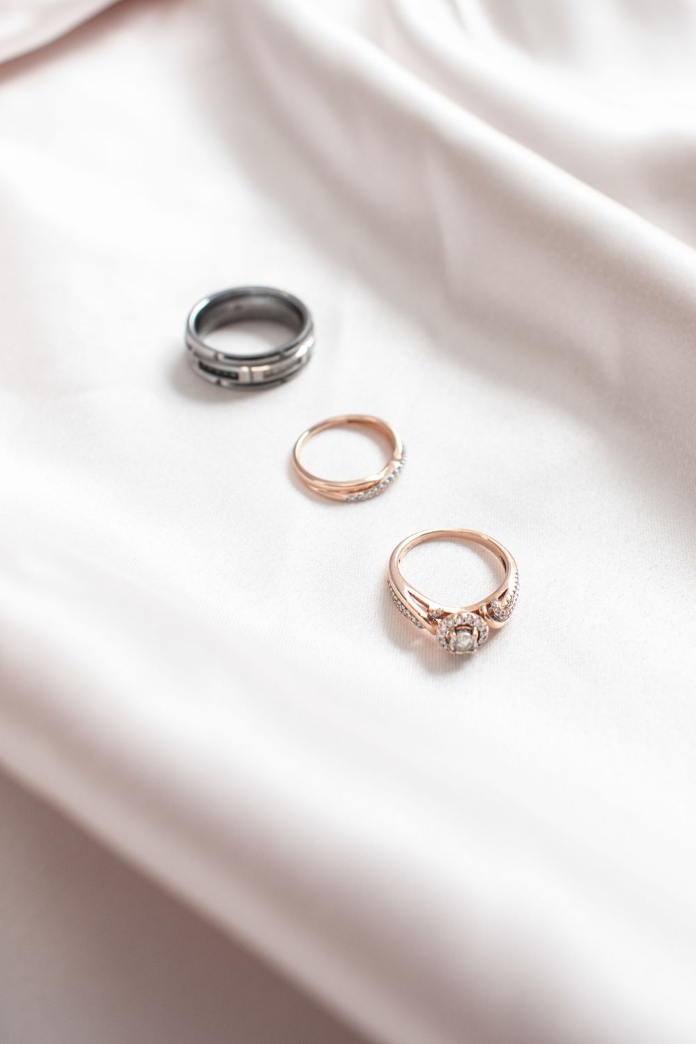 Three elegant rings including black and rose gold bands with a sparkly engagement style ring on white silk fabric.