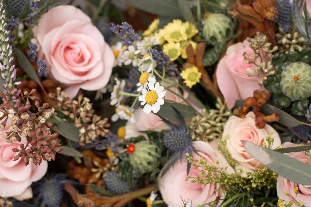 Close-up view of a romantic floral arrangement with pale pink roses, white daisies and rustic dried elements.