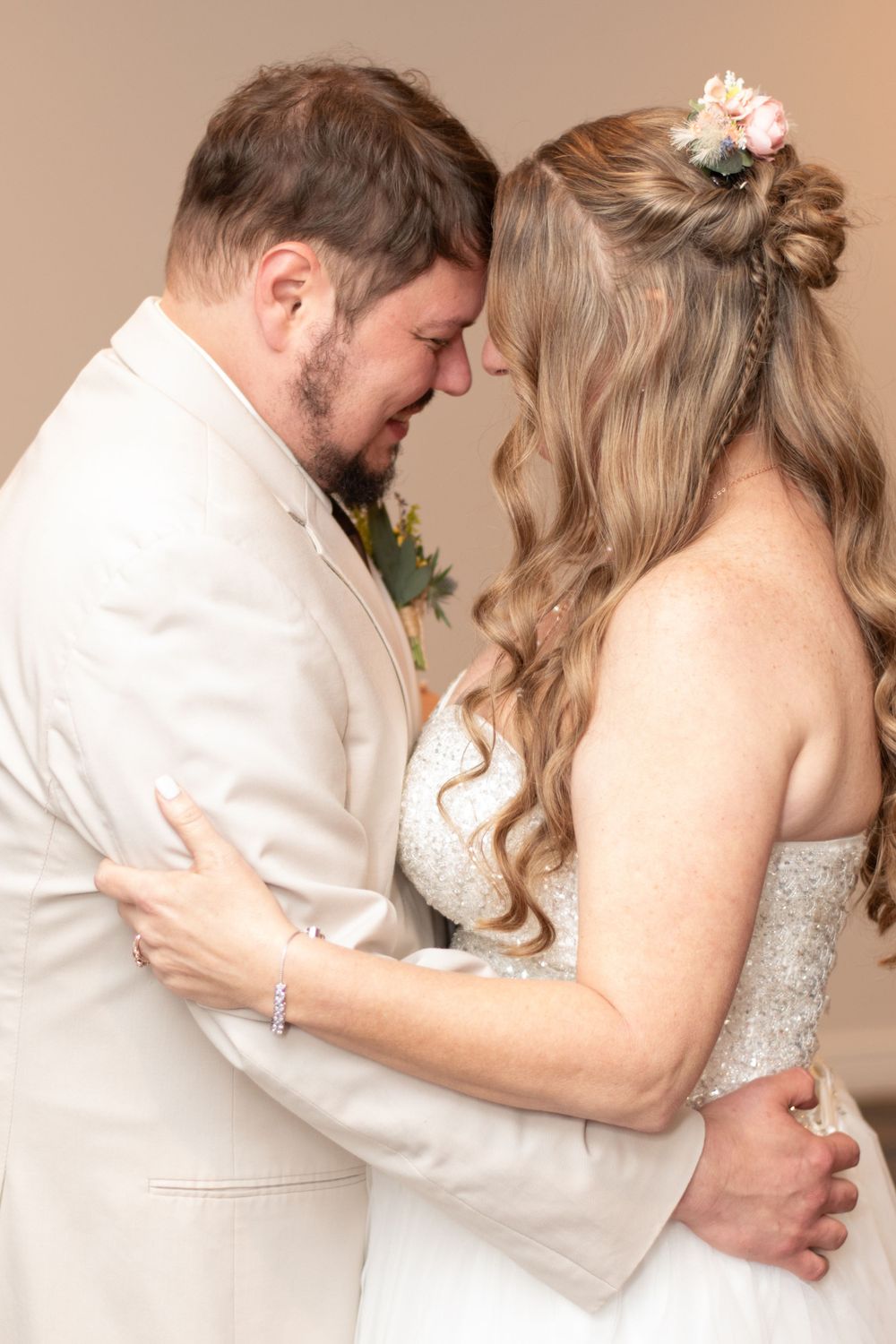 A romantic wedding moment showing a couple in cream and white formal attire embracing during their special day.