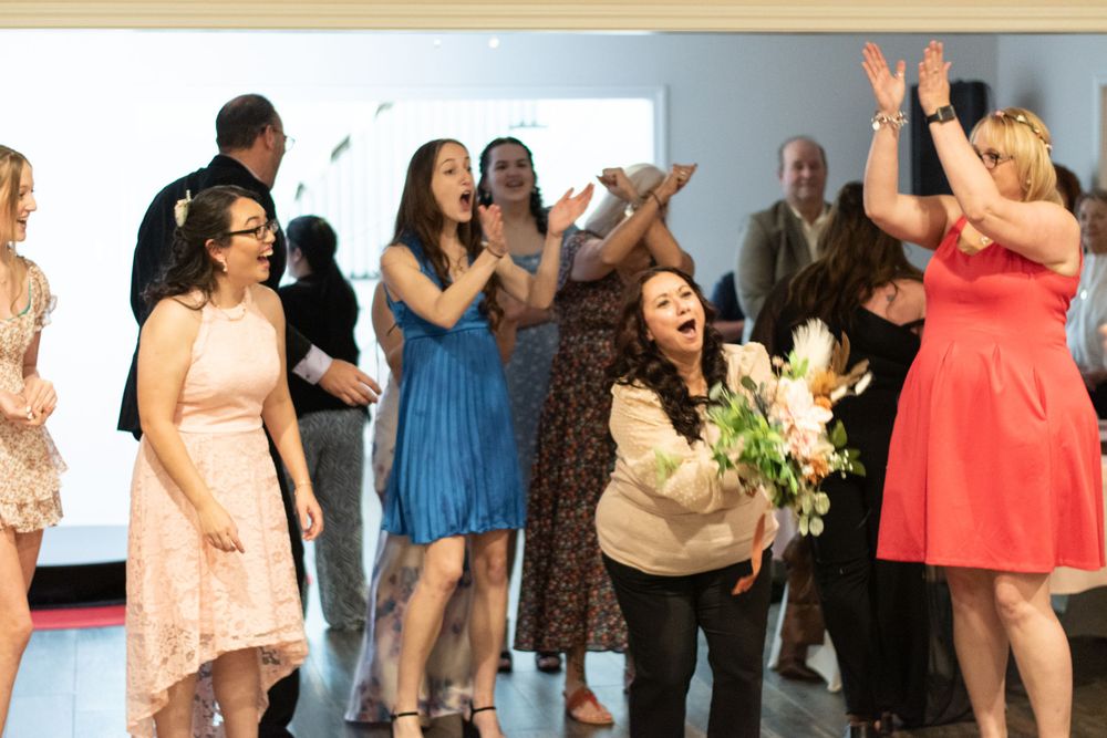 A group of people celebrating with raised arms and flowers, wearing colorful dresses in pink, blue and coral.