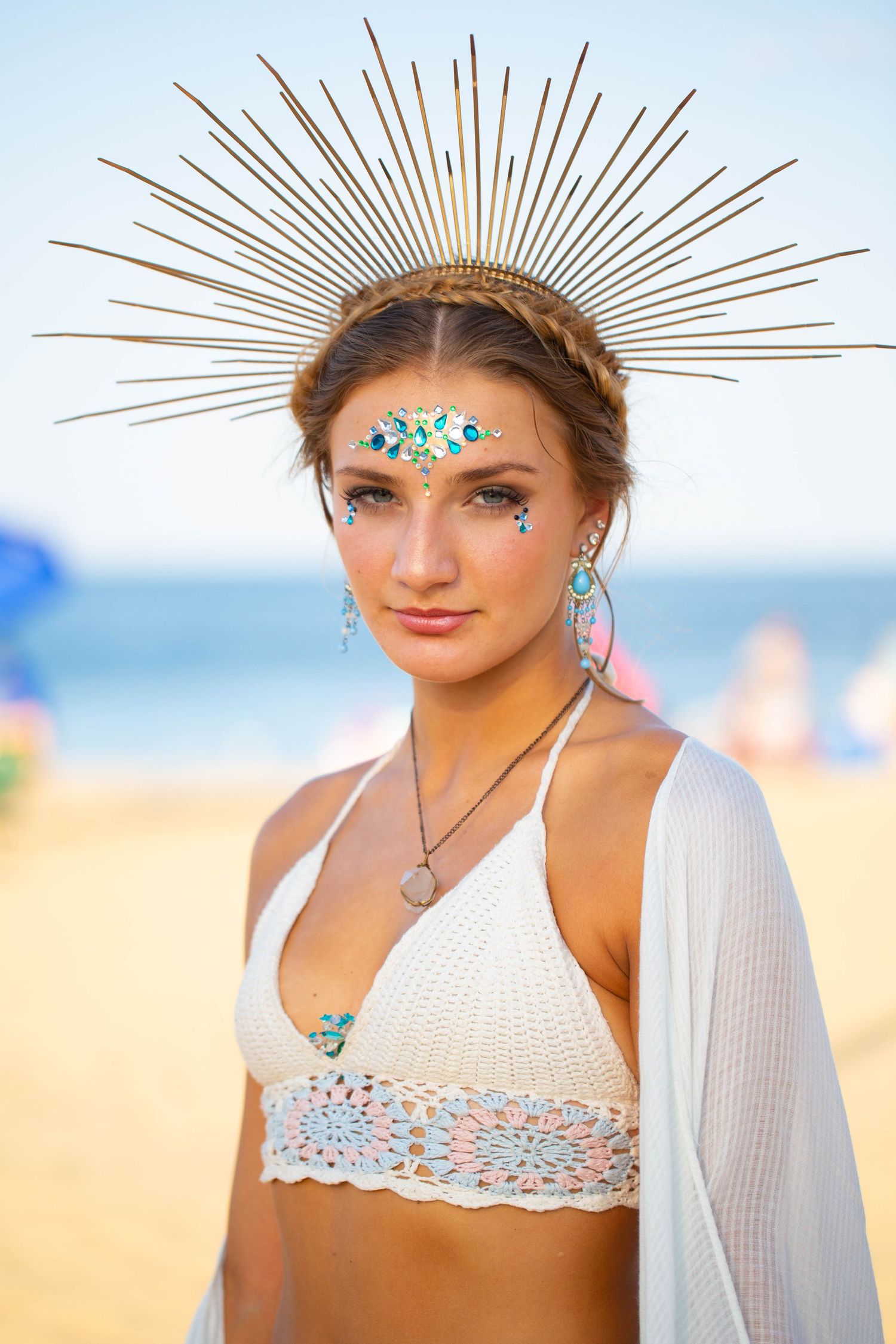 Festival-goer on beach wearing sunburst crown and sparkly face decorations.