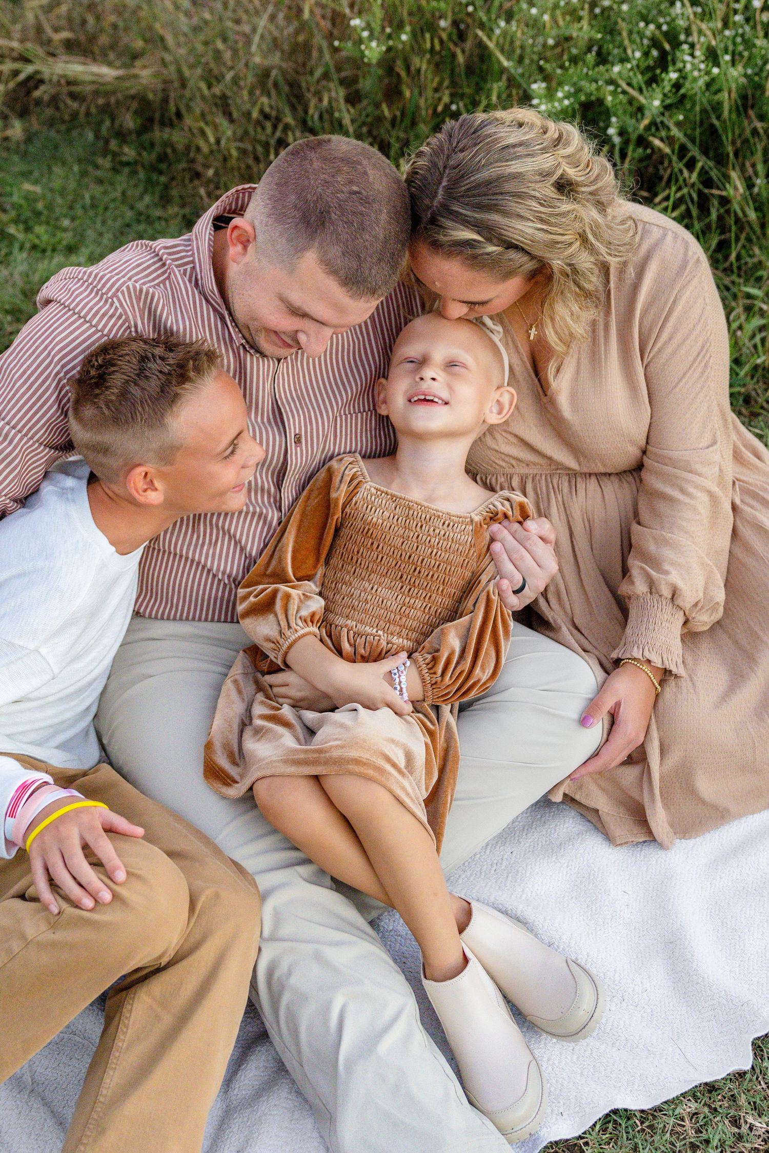 A family shares a joyful moment together while sitting on a blanket outdoors in coordinated autumn-toned outfits.