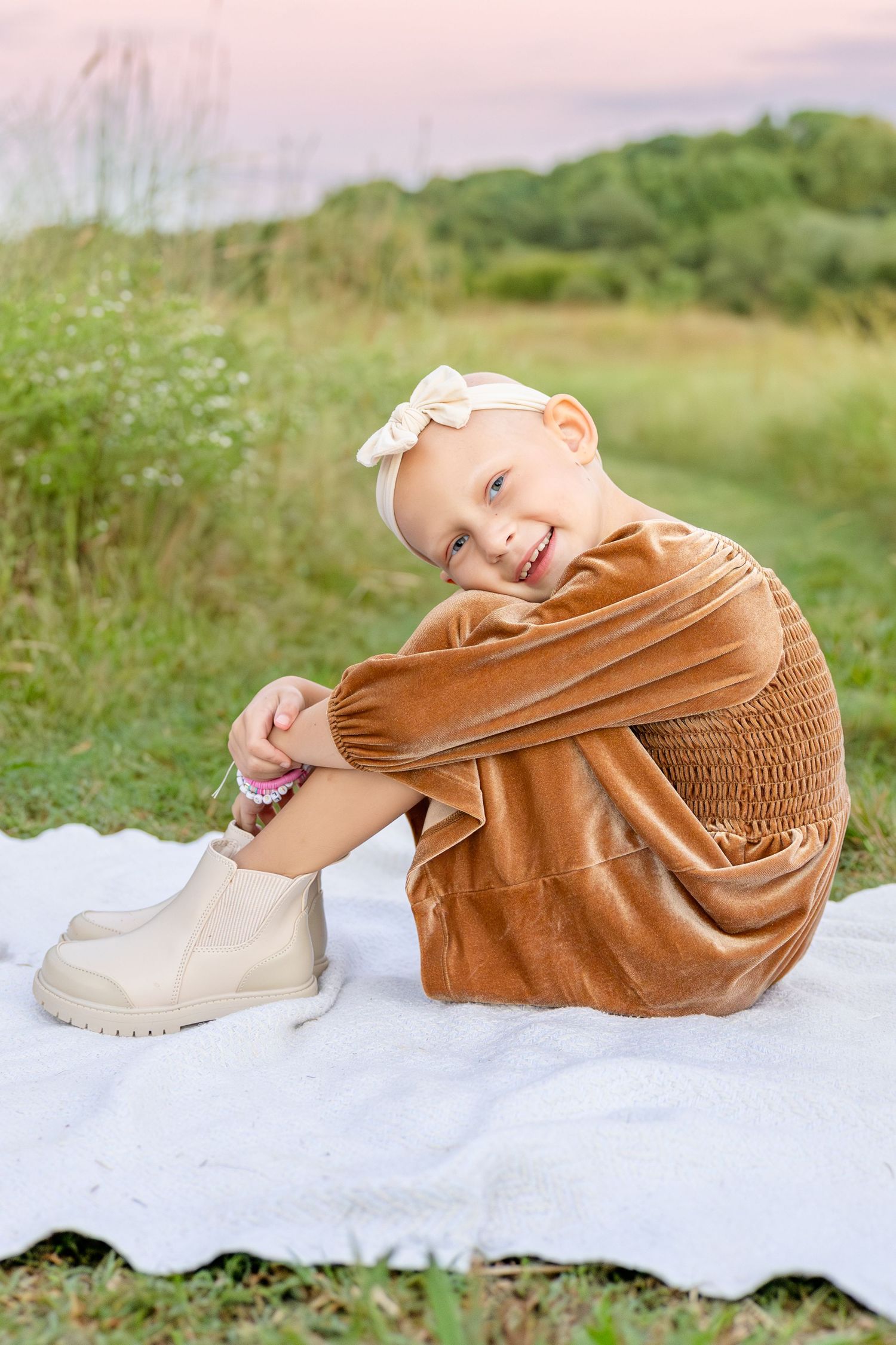 A joyful portrait in a brown dress and boots sitting on a white blanket in a green meadow at sunset at the NC Museum of Art in Raleigh.