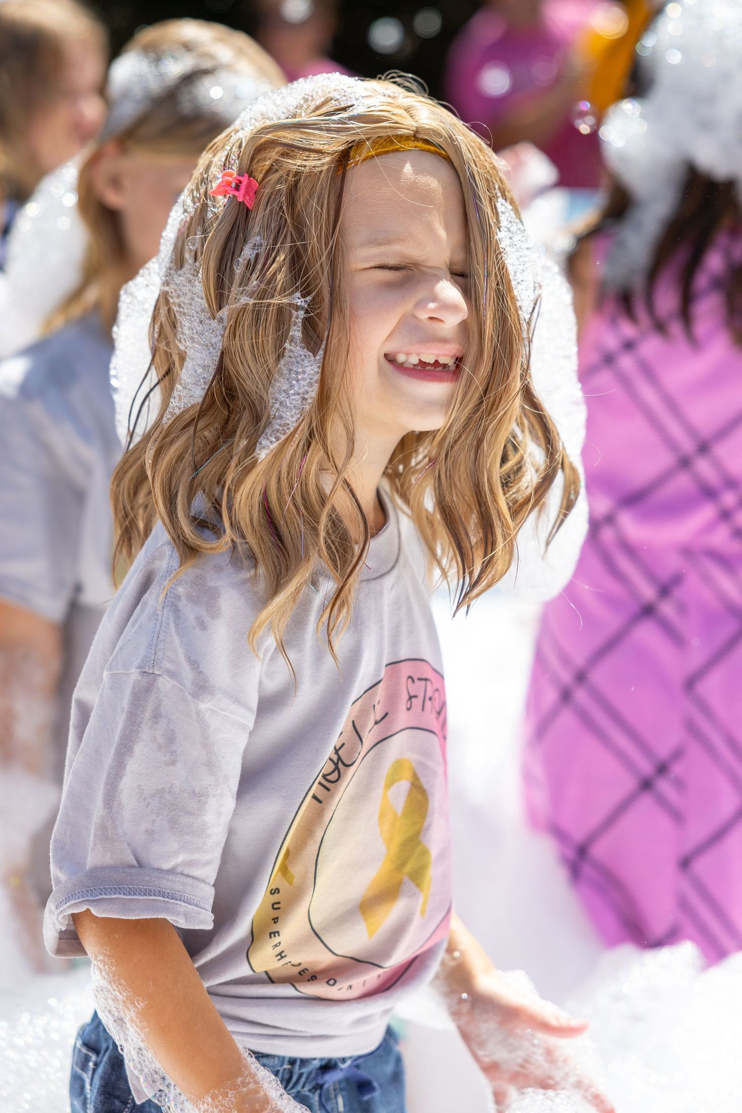 A girl in a white shirt with wavy blonde hair and sunlight streaming in dances joyfully against a pink bokeh background.