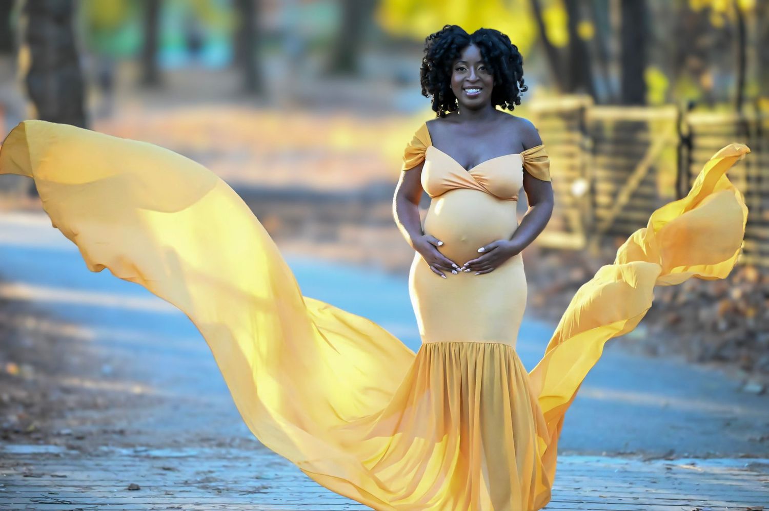 Pregnant woman in a flowing golden yellow gown photographed near water during a dramatic outdoor maternity session in New York. maternity