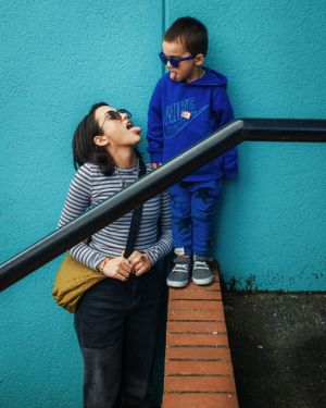 Fun candid moment in front of a bright turquoise wall with someone in sunglasses and a blue hoodie standing on steps.