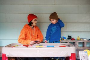 Two people in winter hats doing crafts at a small table with art supplies and toys.