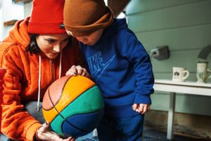 Two children in winter coats lean in together to examine a colorful basketball.
