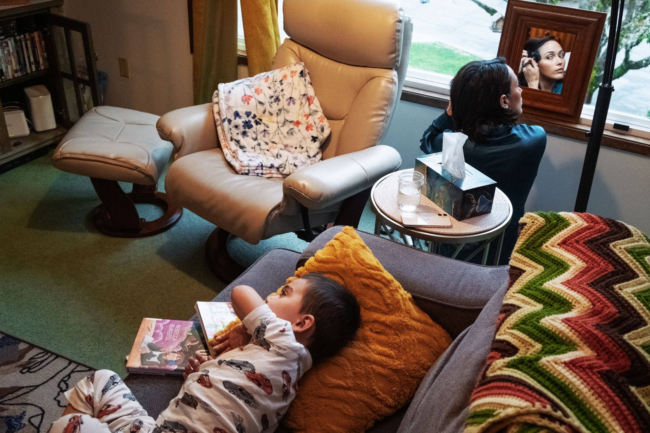A cozy living room scene with a tan recliner, colorful zigzag throw, and scattered pillows beside a window.