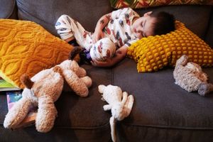 A cozy scene of relaxation on a gray couch with stuffed animals and a yellow knit pillow.