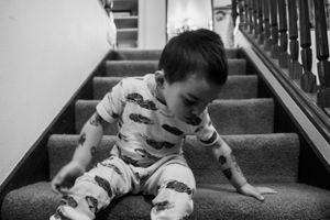 A child in dinosaur print pajamas sits on carpeted stairs in black and white tones.