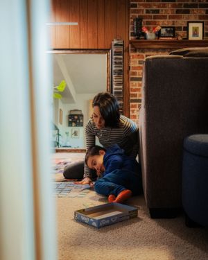 Two figures reading together in a cozy corner with exposed brick walls and carpet.