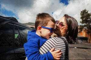 A tender moment shared between parent and child wearing sunglasses in a parking lot on a sunny day.