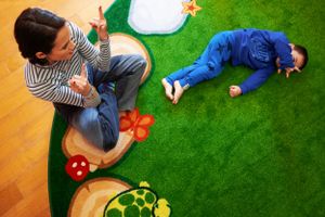 Two children lay on contrasting orange and green floor surfaces with decorative mushroom and flower accents.