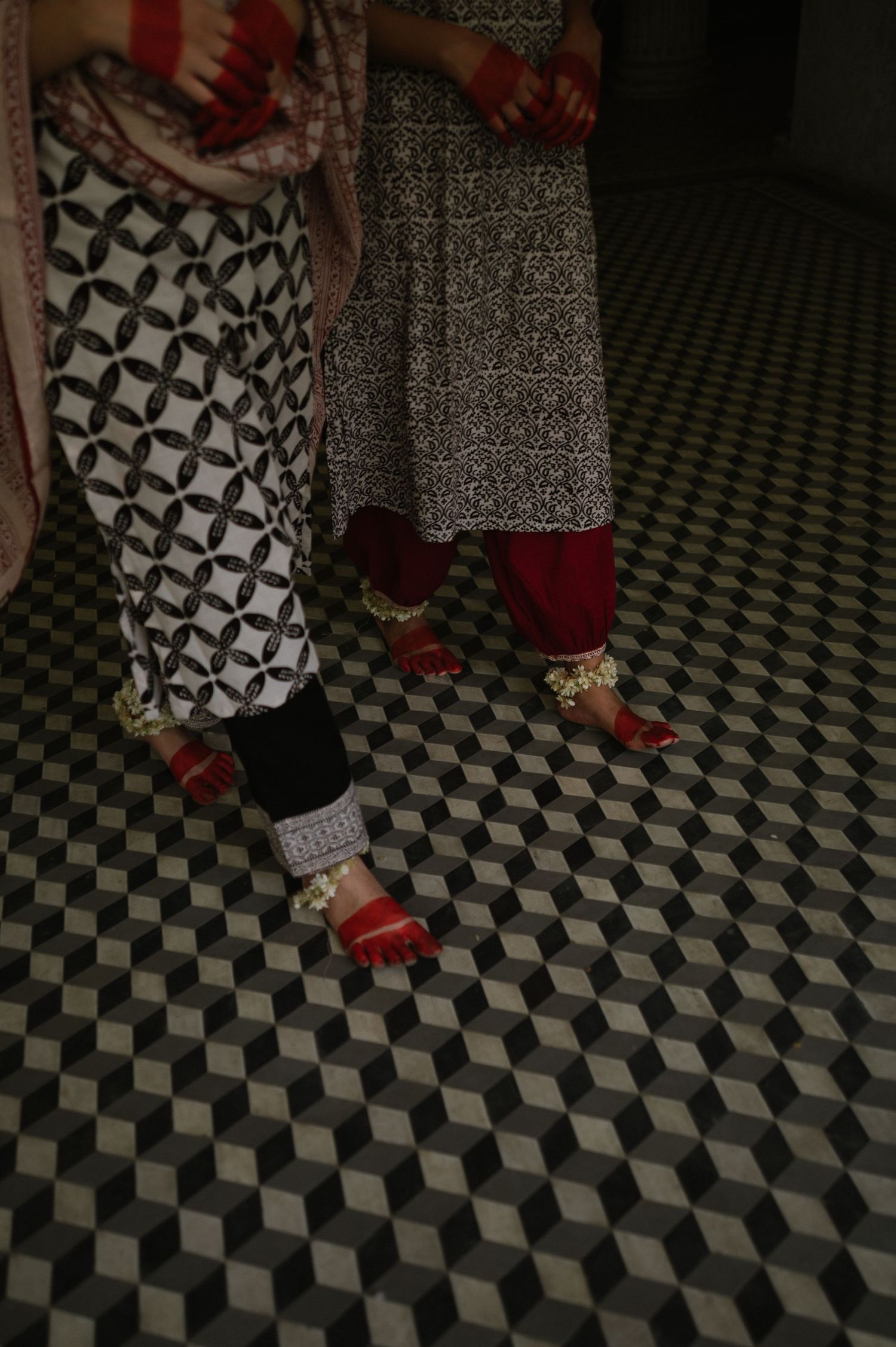 Close-up of feet wearing traditional Indian anklets on geometric tile floor pattern.