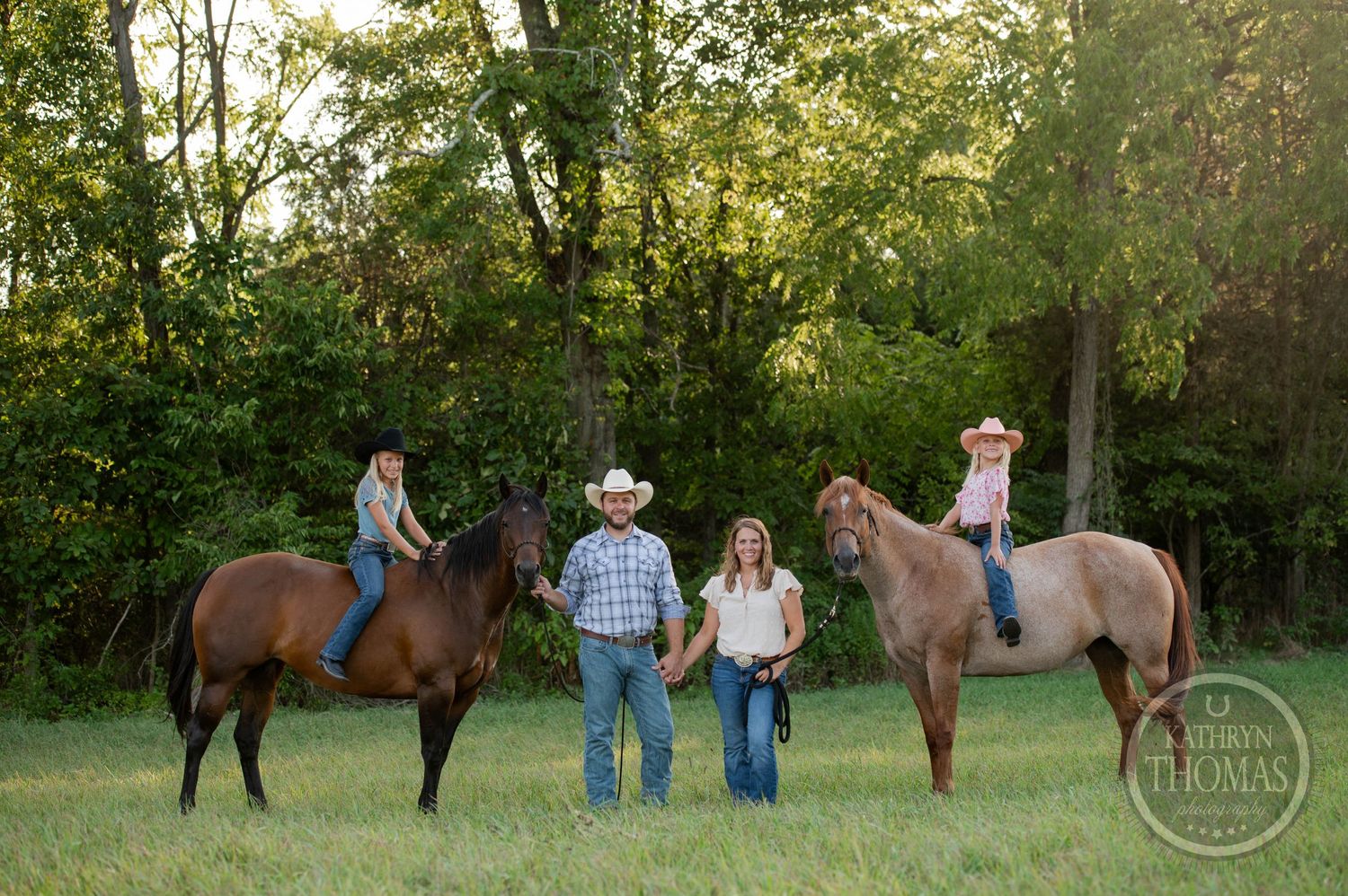 Two horses and riders pose for a family photo in a pastoral setting.