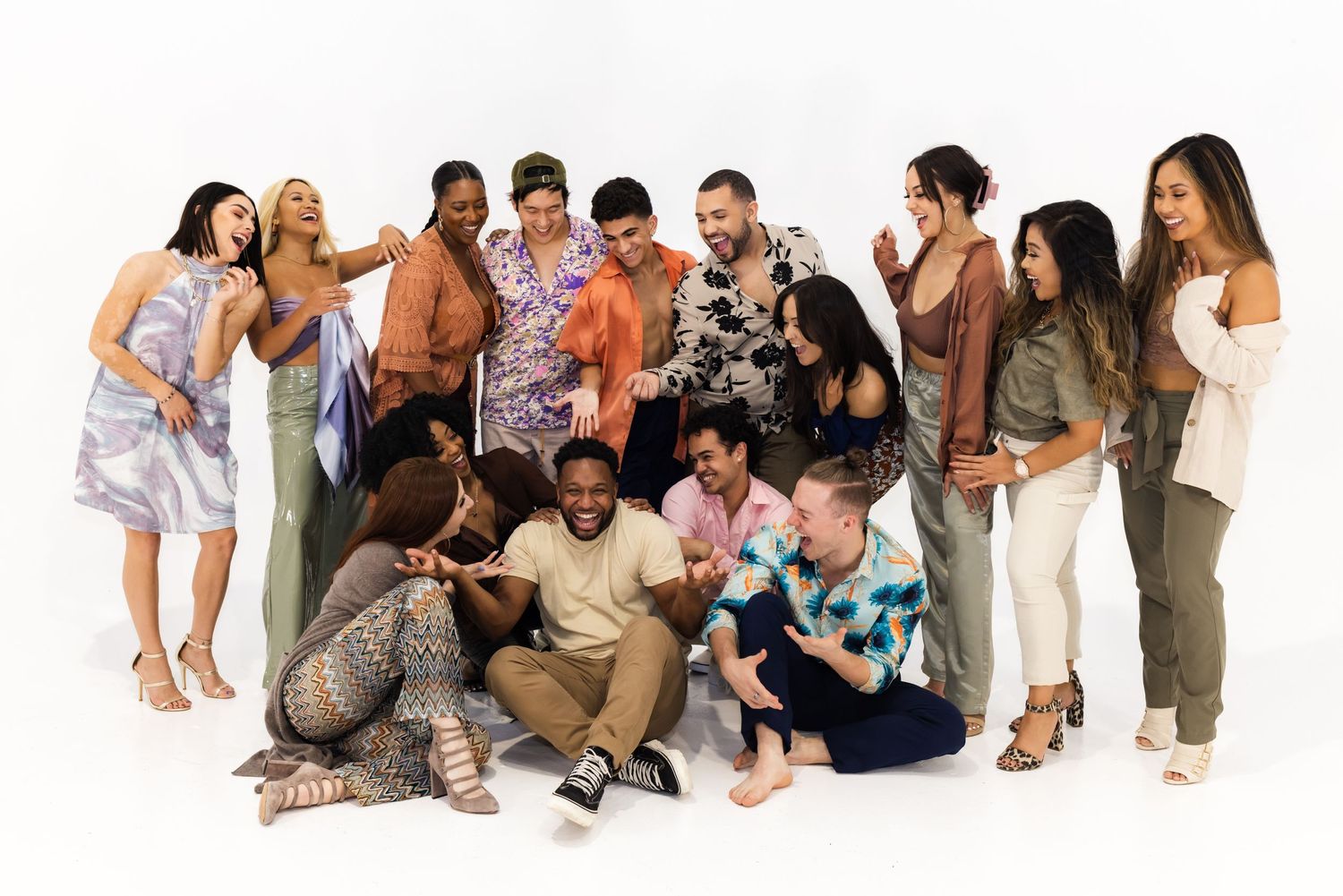 Diverse group of people gathered closely together in casual clothing posing and laughing against a white background.
