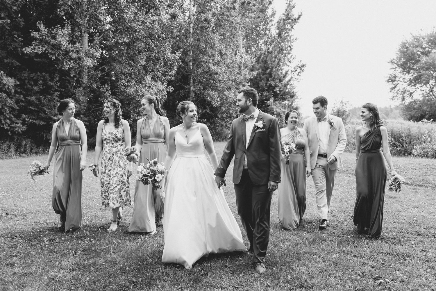 Wedding party walks together on grass in elegant black and white photograph.