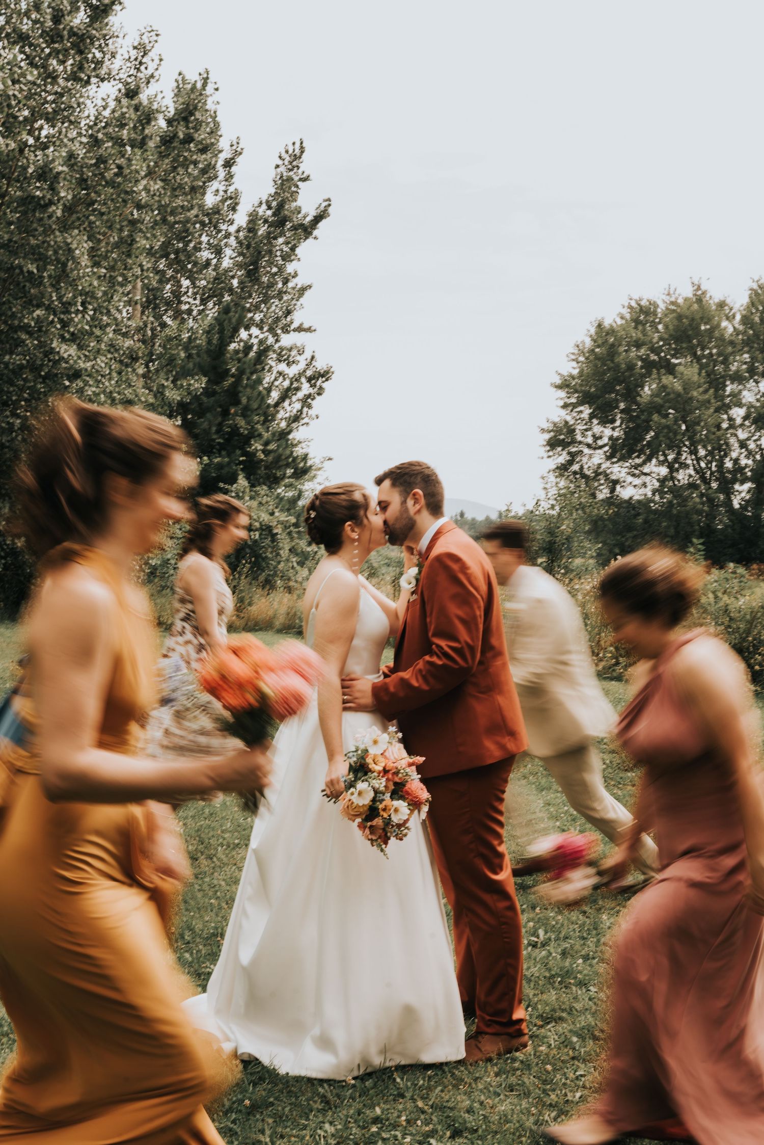 Wedding party celebrating with joyful movement as couple shares romantic moment in outdoor garden setting at sunset.