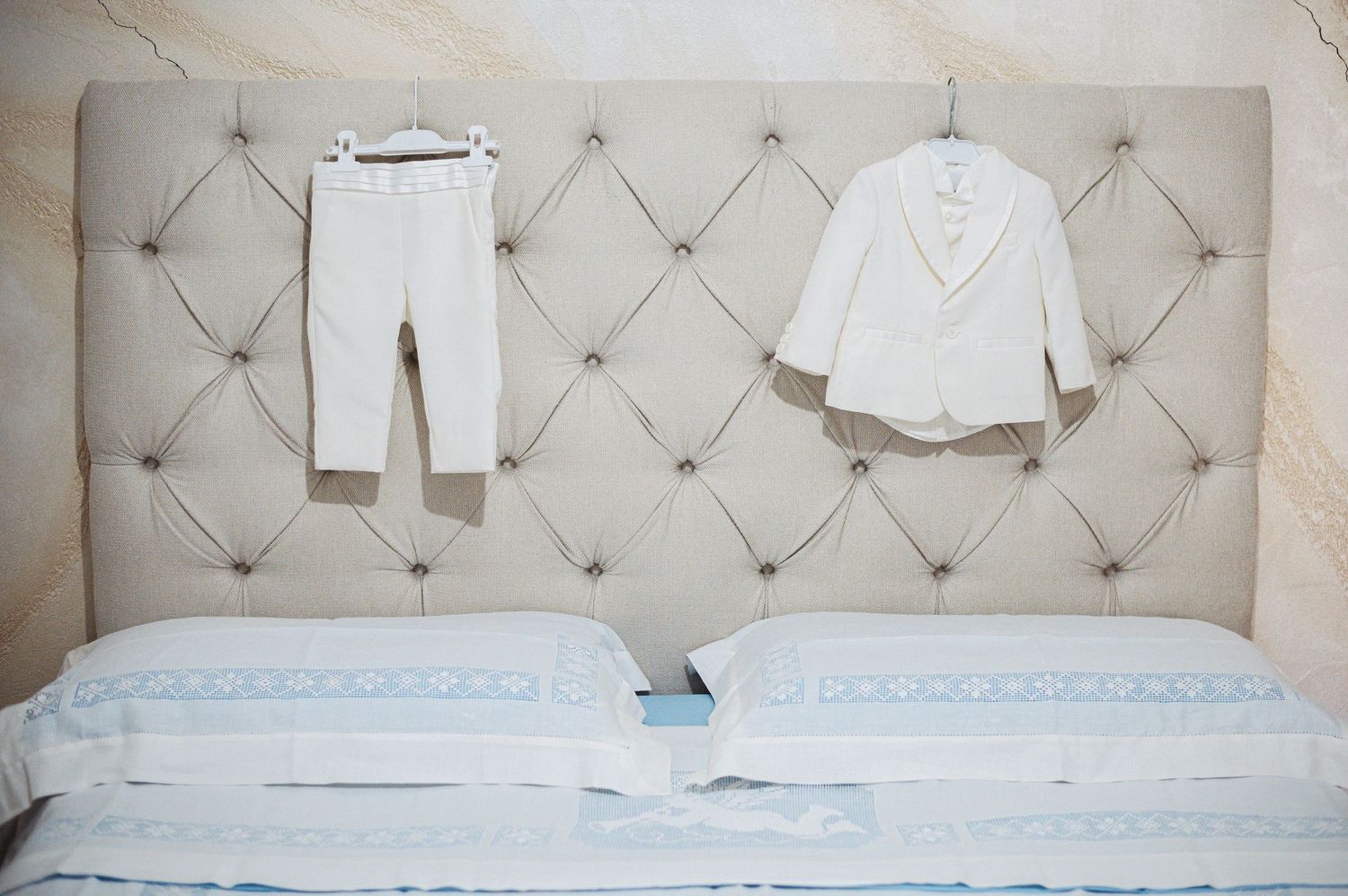 White formal children's outfit displayed on tufted headboard of bed.