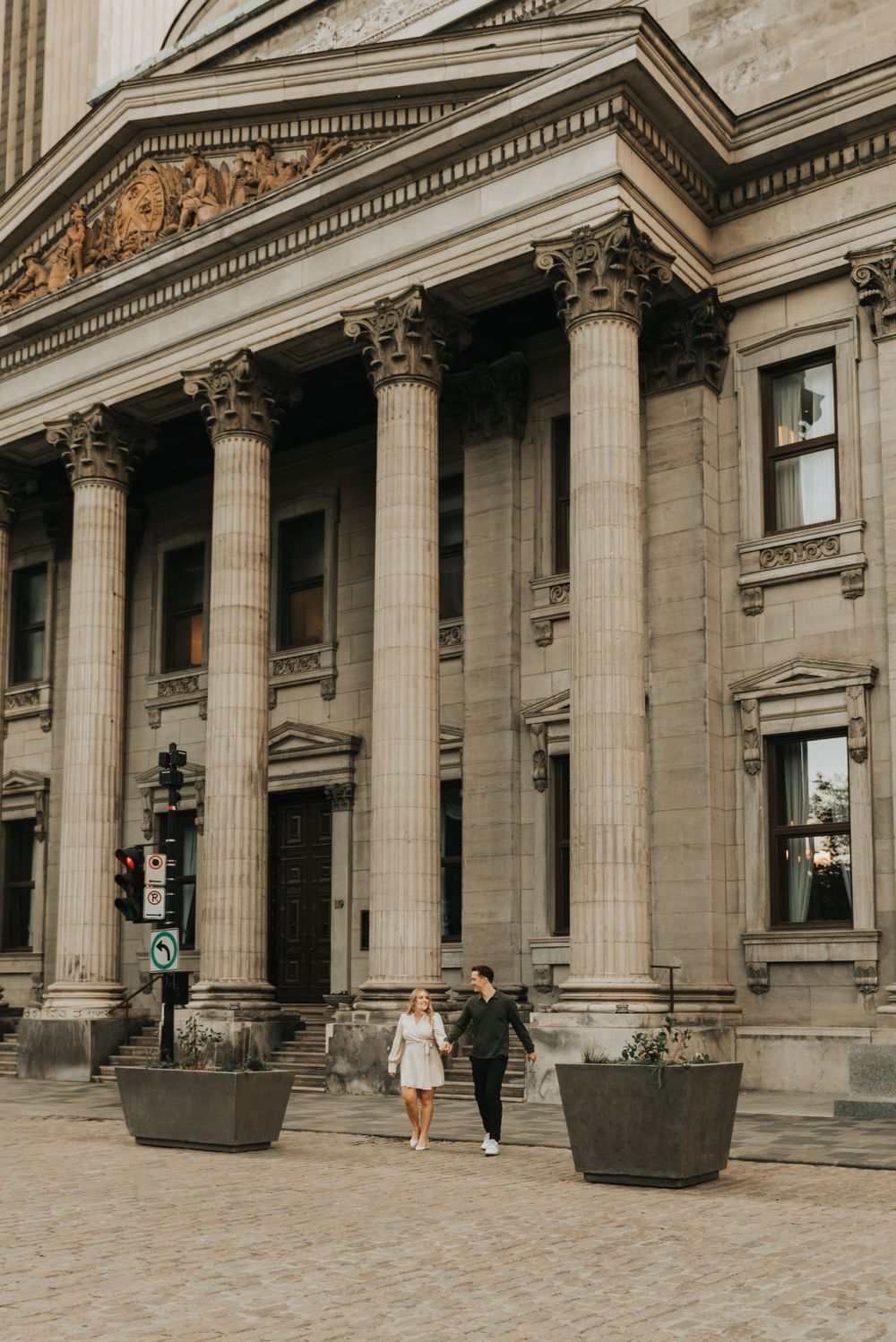 Couple walks outside a grand neoclassical building with tall Corinthian columns and ornate architectural details.