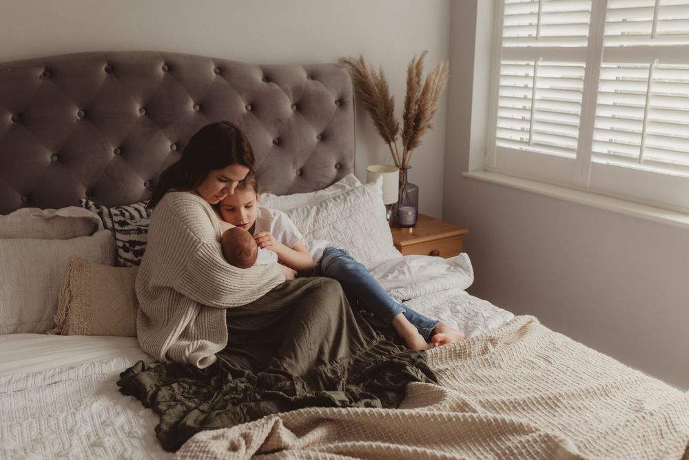 Mother cradling newborn baby while sitting on bed in cozy bedroom.